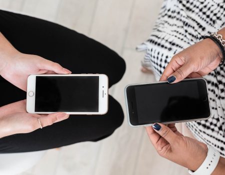 Two women seated holding phones with black screen facing up